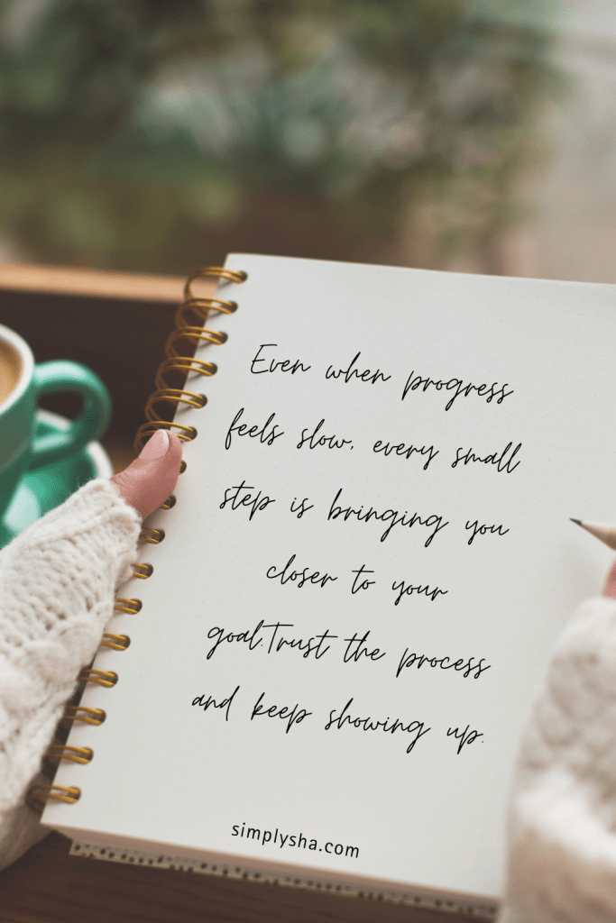 A cozy scene of a person holding a notebook with a handwritten quote that reads, “Even when progress feels slow, every small step is bringing you closer to your goal. Trust the process and keep showing up.” A cup of coffee sits nearby, creating a calm and motivational atmosphere.