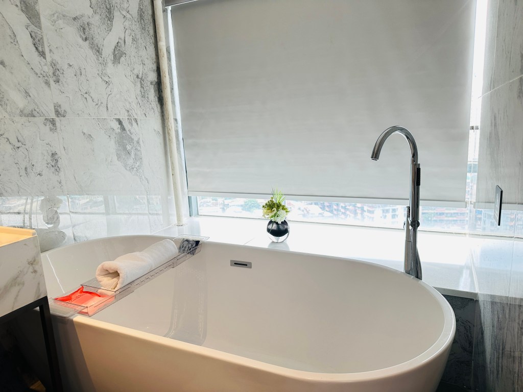 Freestanding bathtub in a marble bathroom with a window overlooking the Guangzhou city skyline.