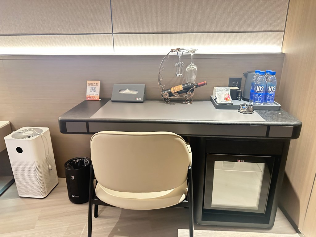 Desk area with minibar, wine rack, complimentary water, and air purifier inside a hotel room in Guangzhou, China.