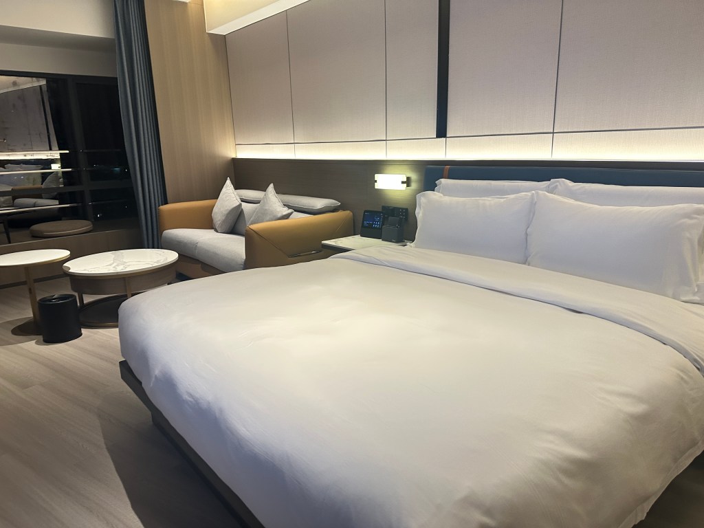 Spacious hotel room in Guangzhou with a king bed, sofa seating area, and soft ambient lighting.