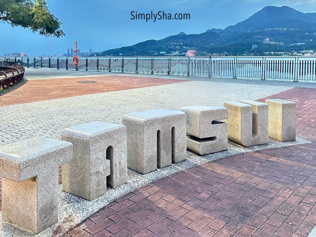 Tamsui sign along the riverside promenade with mountain and river views in the background