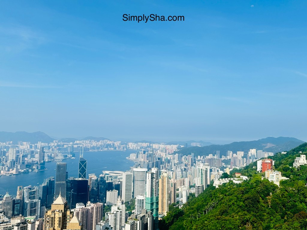 Panoramic view of Hong Kong’s skyline and Victoria Harbour surrounded by green hills from Victoria Peak.