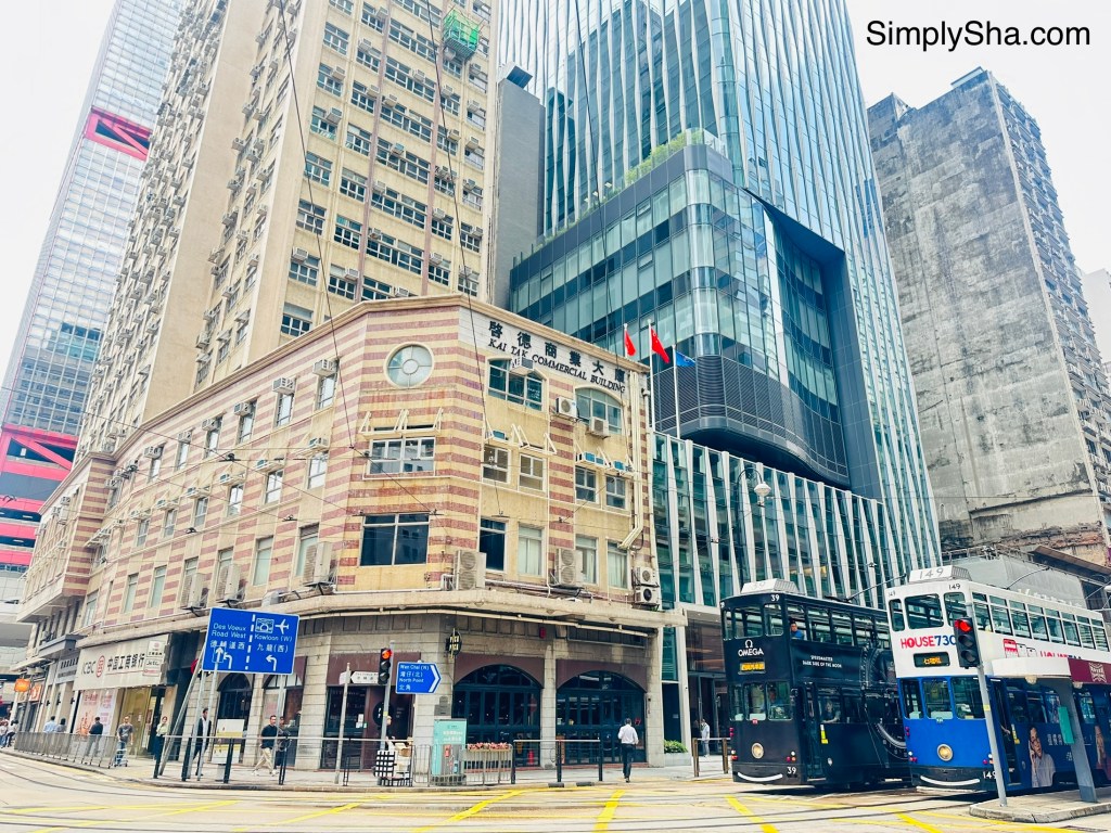 Street view of Sheung Wan, Hong Kong, featuring historic buildings, modern skyscrapers, and a blue Ding Ding Tram.