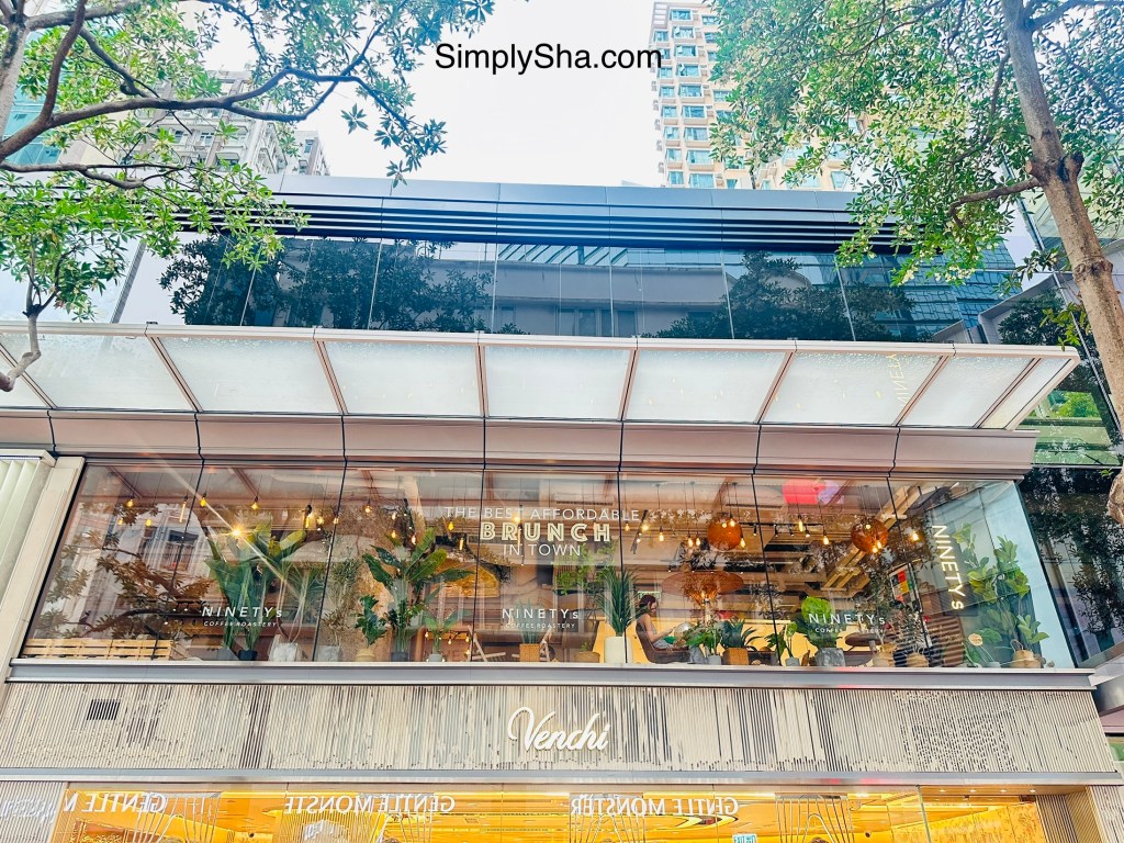 Modern glass-fronted building with shops and restaurants surrounded by trees in Causeway Bay, Hong Kong.